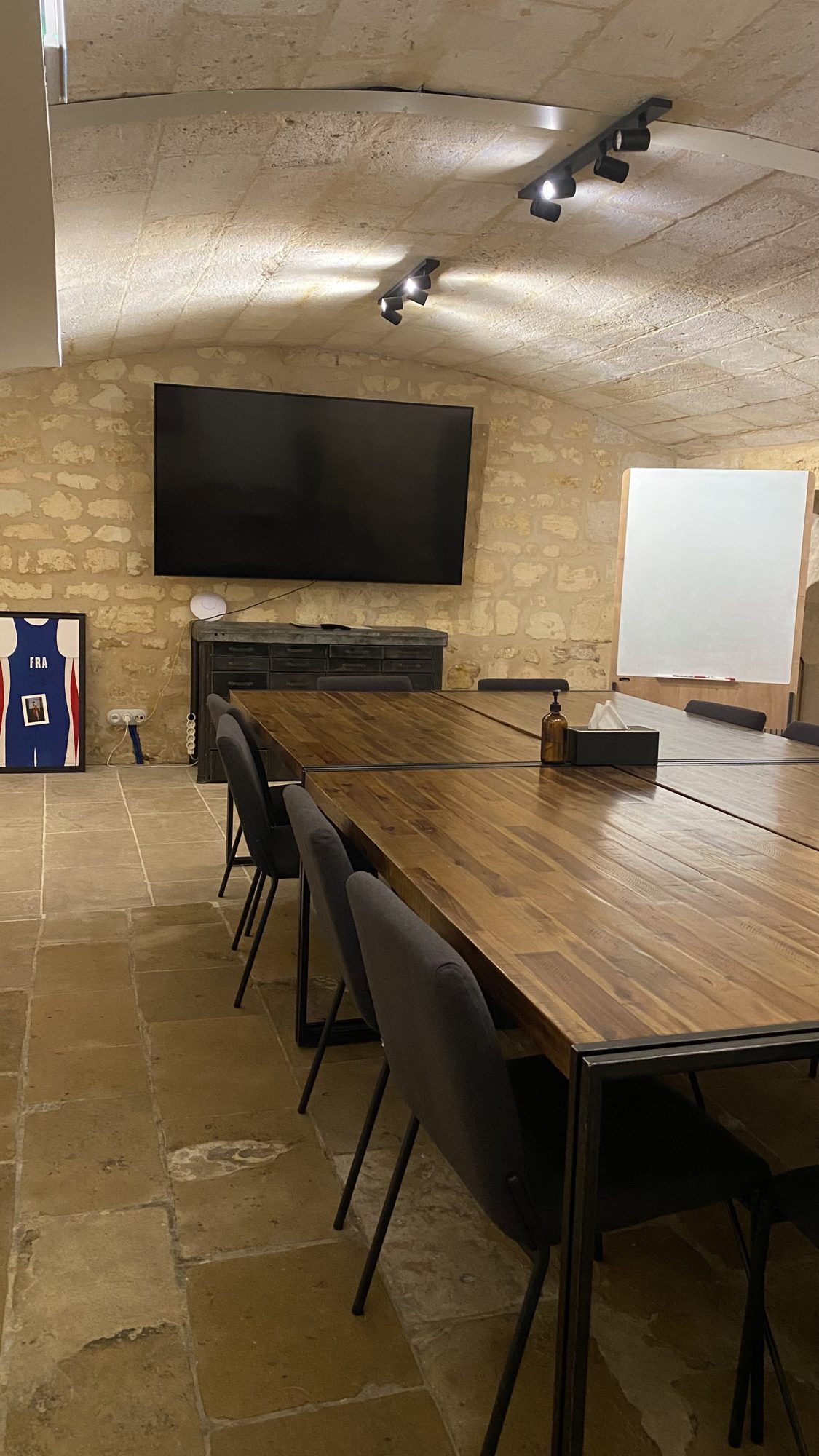 Cave voûtée en pierre aménagée en salle de réunion avec grande table et écran